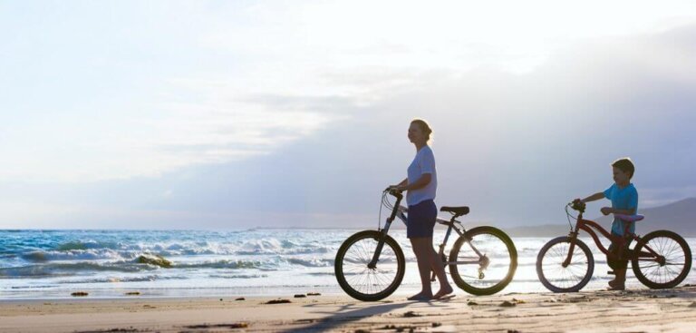 Due persone camminano con le biciclette su una spiaggia al tramonto.