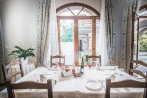 Tavola apparecchiata in una sala da pranzo con vista sul giardino attraverso ampie finestre.