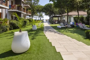 Percorso pedonale in un giardino ben curato con palme e sedie a sdraio vicino a edifici e alberi.