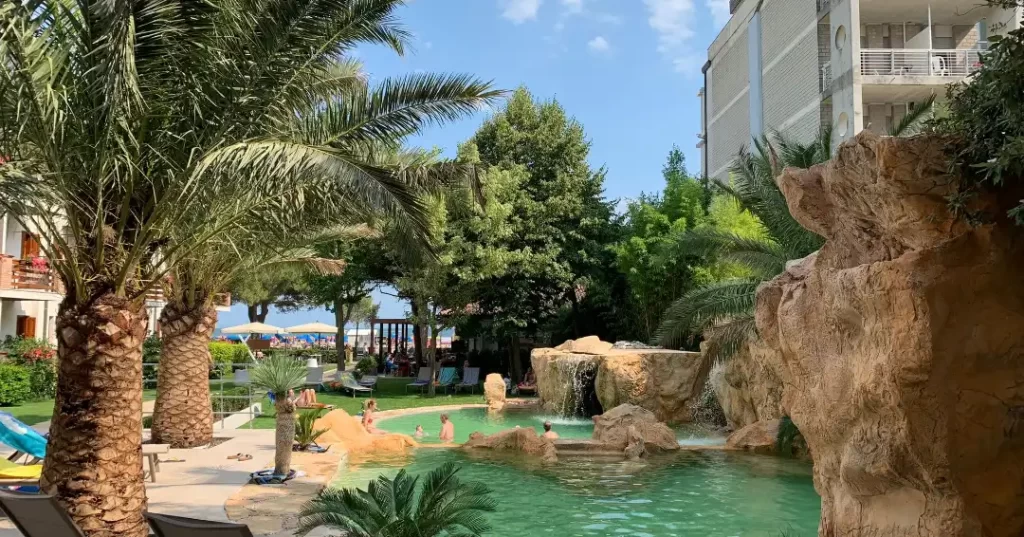 Piscina all'aperto circondata da palme e rocce in un contesto alberghiero.