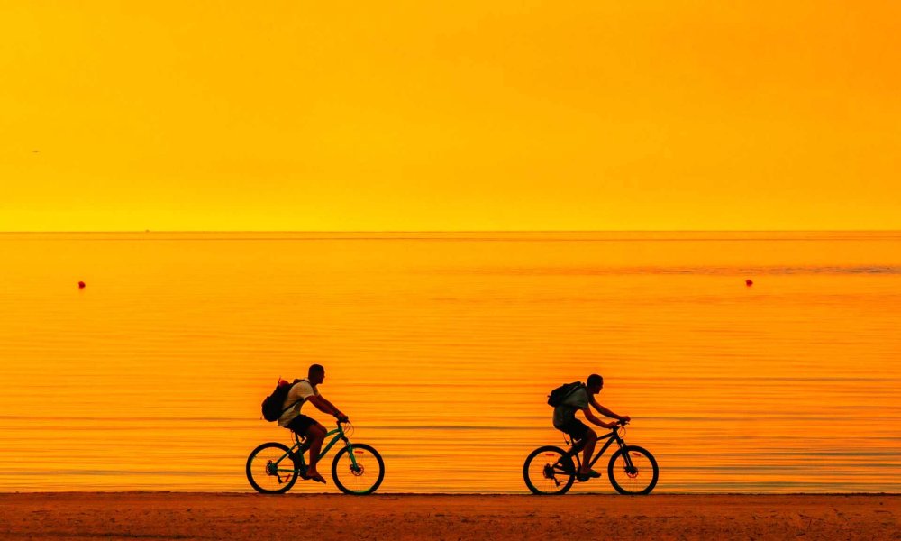 Due persone in bicicletta lungo una spiaggia al tramonto.