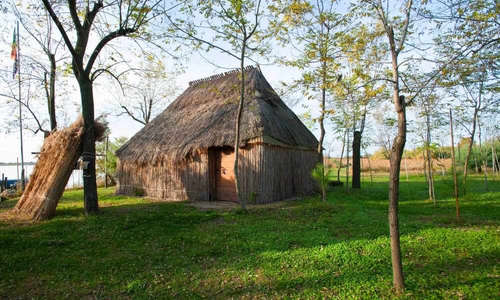 Capanna di paglia tradizionale in un paesaggio alberato e verde.