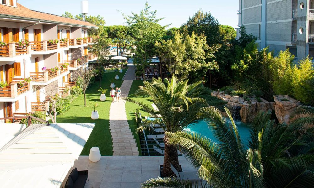 Vista di un hotel con giardino, piscina e terrazze circondato da alberi.